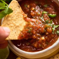 Close up of corn chip scooping up homemade salsa (Salsa recipe - restaurant style)