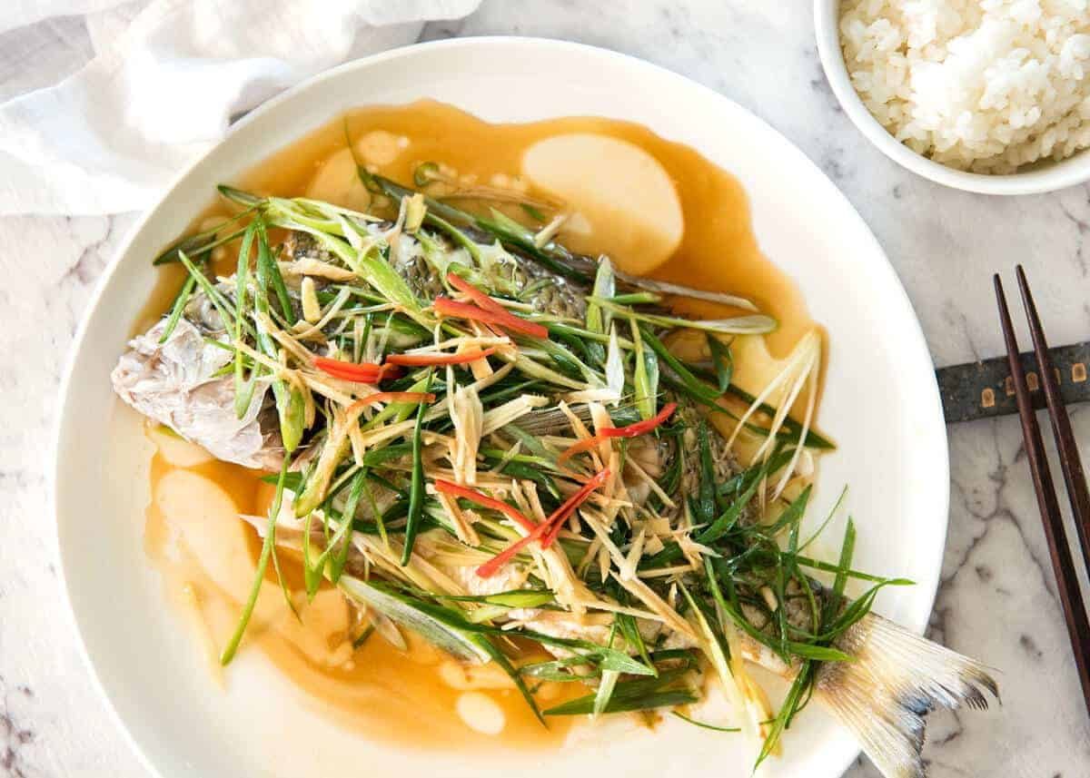 A Chinese Steamed Fish topped with Ginger and Shallots and seasonings, with hot oil poured over it to create a dramatic sizzle and an amazing sauce. So simple, yet so utterly delicious. Steam OR bake the fish! www.recipetineats.com