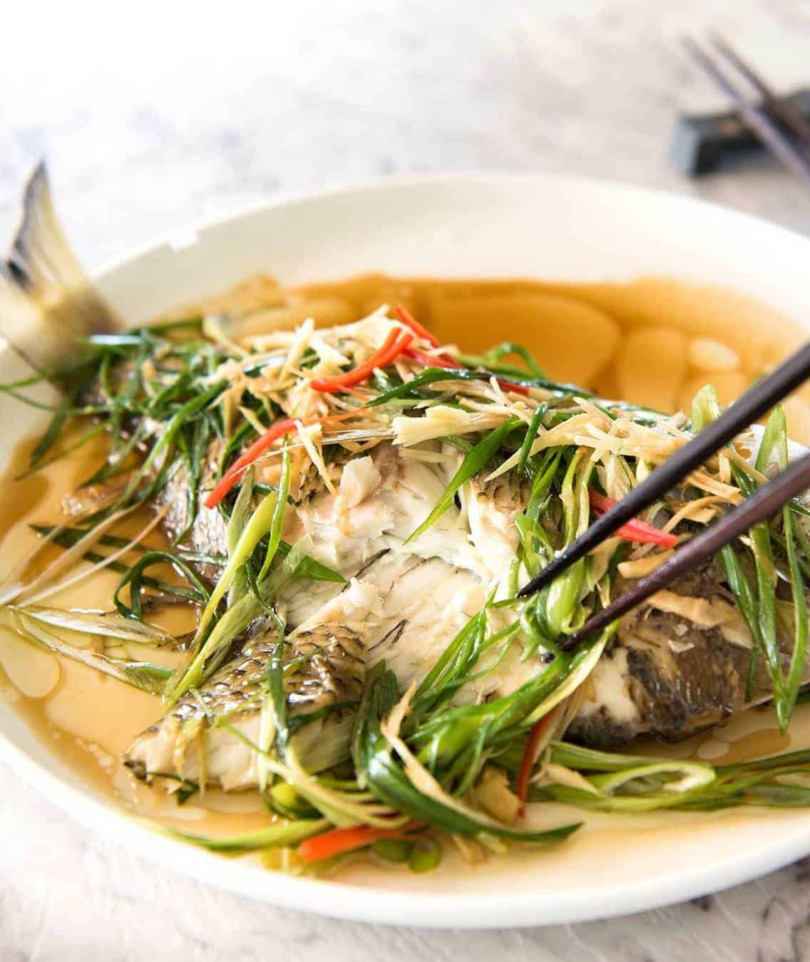 A Chinese Steamed Fish topped with Ginger and Shallots and seasonings, with hot oil poured over it to create a dramatic sizzle and an amazing sauce. So simple, yet so utterly delicious. Steam OR bake the fish! www.recipetineats.com