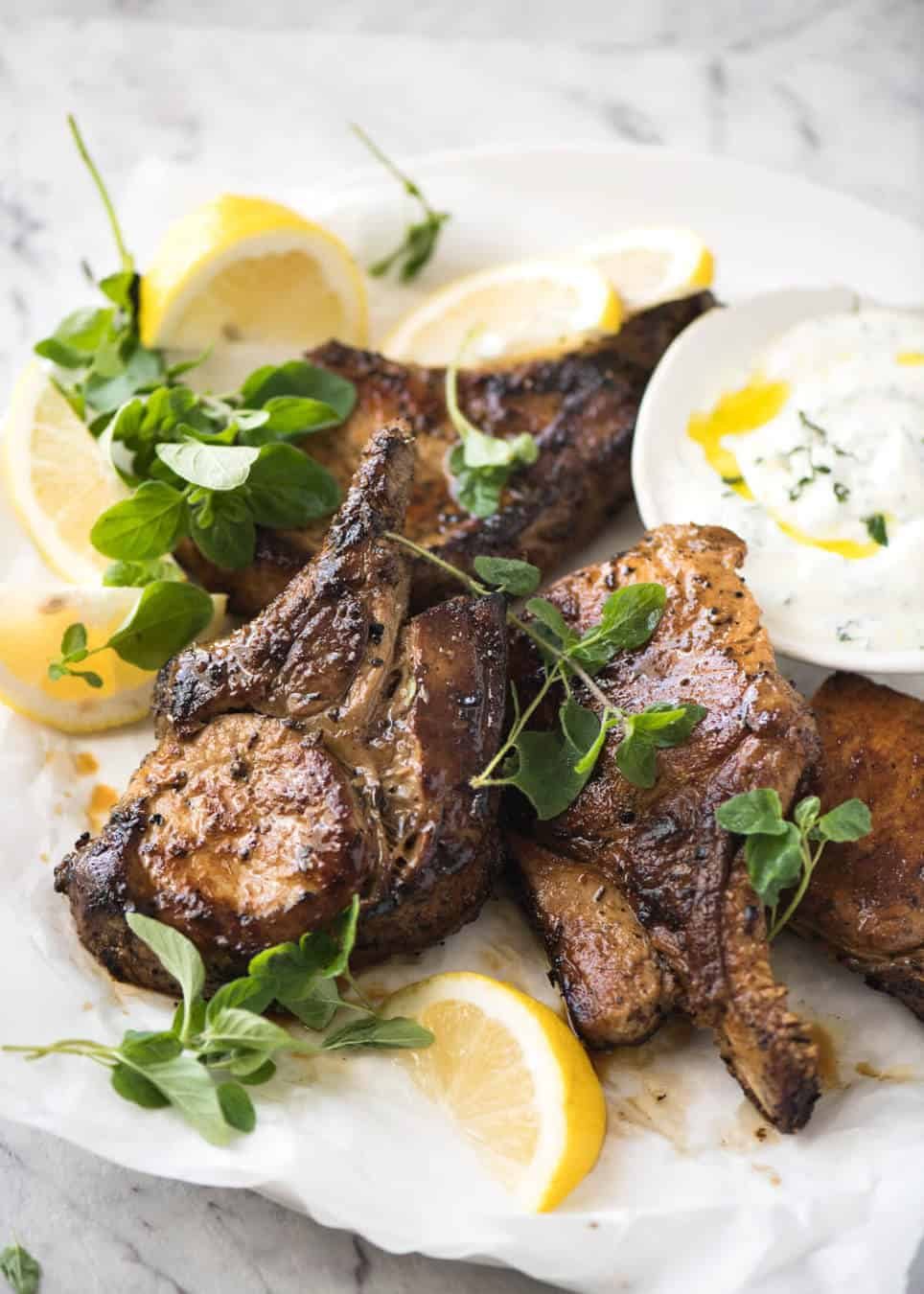 A pile of Lemon Garlic Marinated Grilled Pork Chops on a plate with fresh lemon wedges.