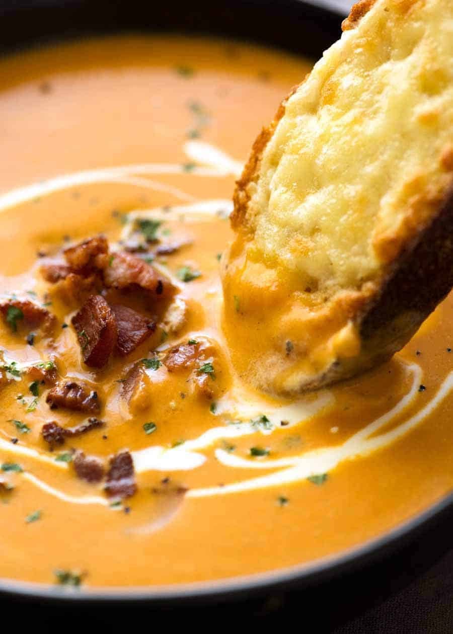 Close up of hot crusty bread being dunked into Carrot Soup in a rustic black bowl.