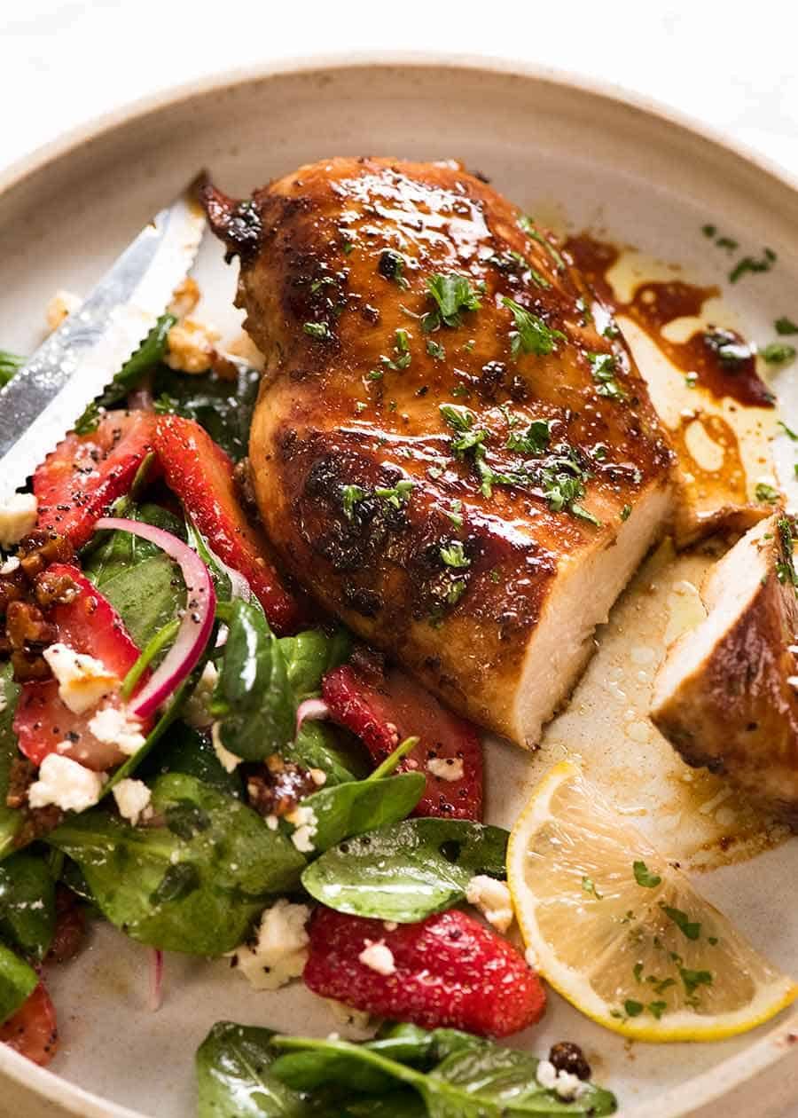 Cooked chicken breast (after marinated in Chicken Marinade) on a white plate with a Strawberry Spinach side salad, ready to be eaten