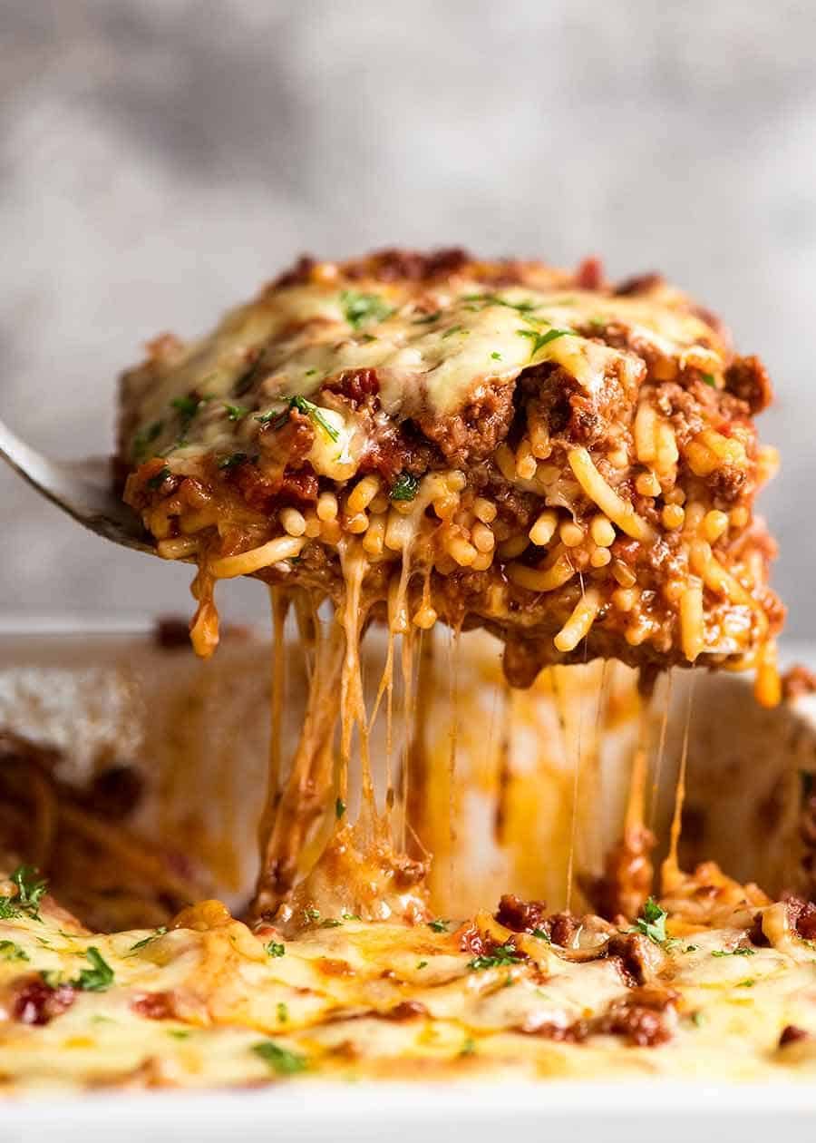 Lifting a cheesy piece of Baked Spaghetti from casserole dish