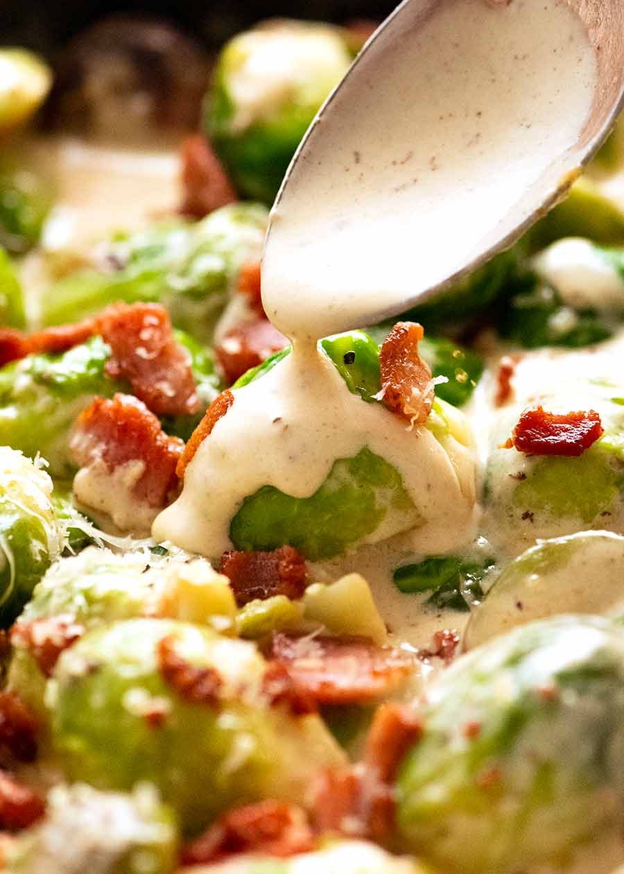 Close up of spoon drizzling creamy sauce over sautéed brussels sprouts